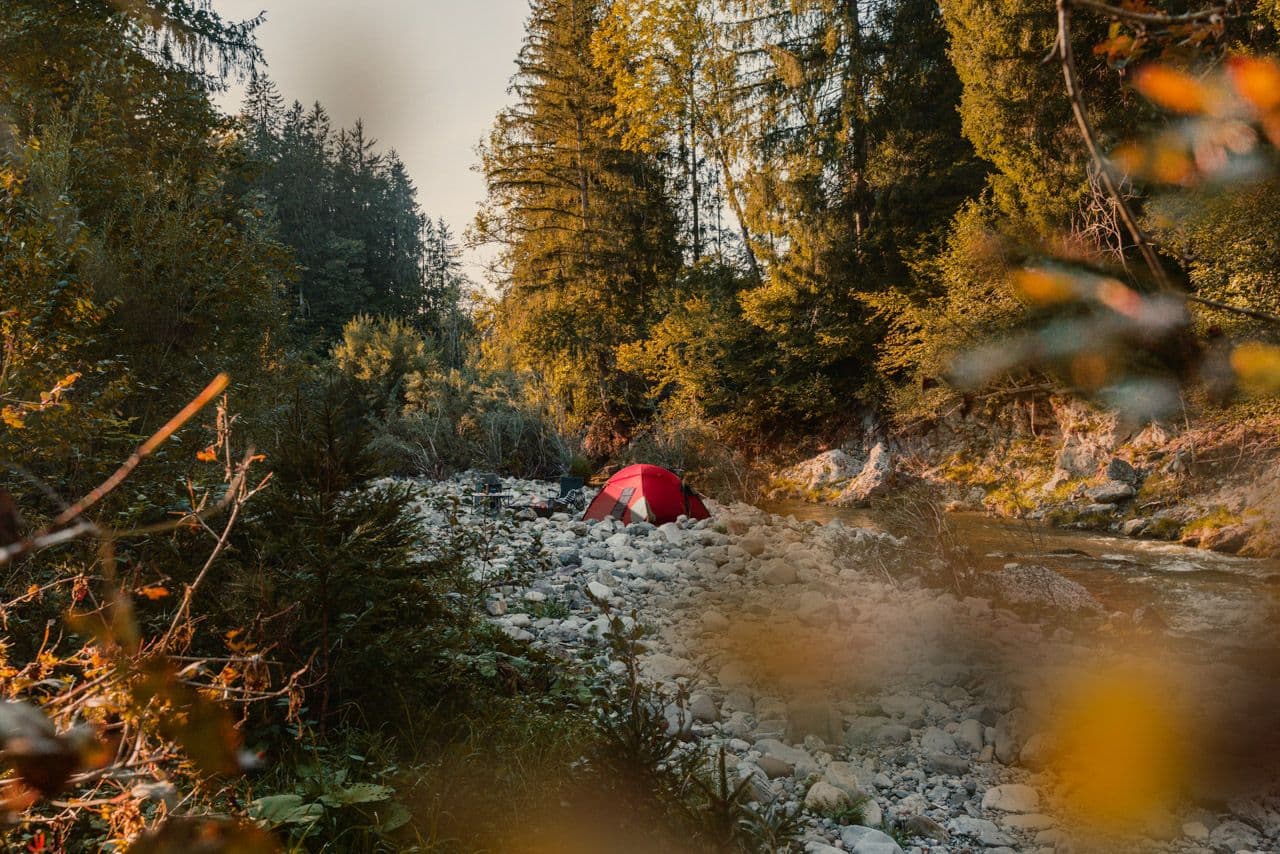 Rotes Zelt am steinigen Bachufer im herbstlichen Wald