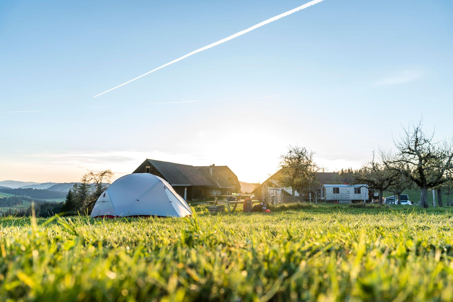 Zelt auf einer Wiese neben einem Bauernhof im Abendlicht