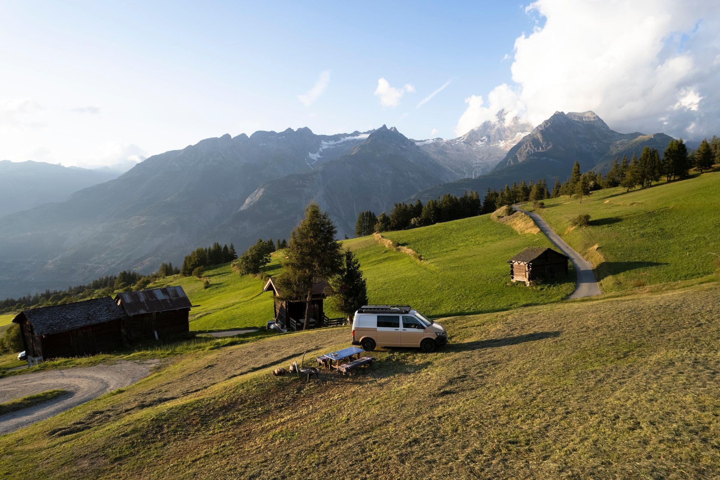 Campervan auf einer Alpwiese mit Holzstadeln vor Walliser Bergen